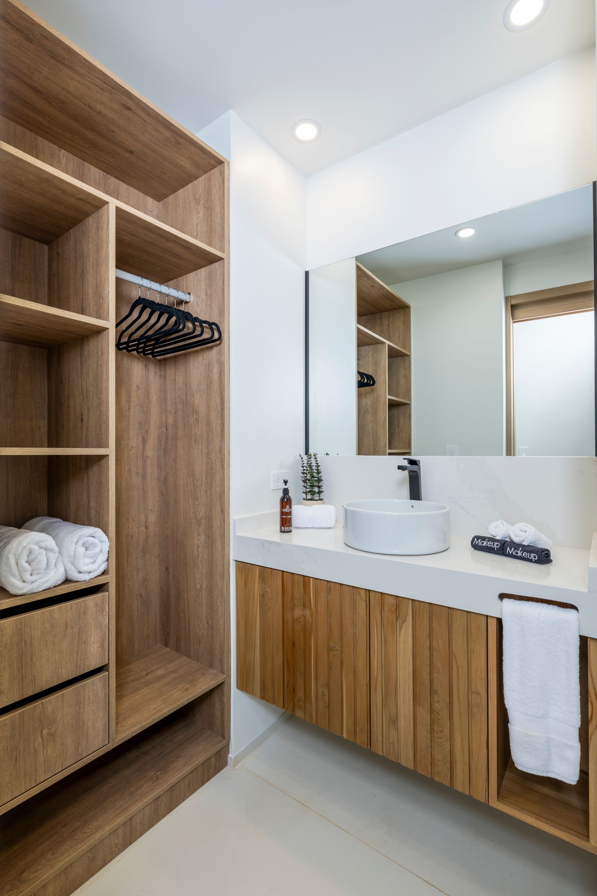 Modern bathroom with wood cabinetry, large mirror, white sink, and towels on open shelving