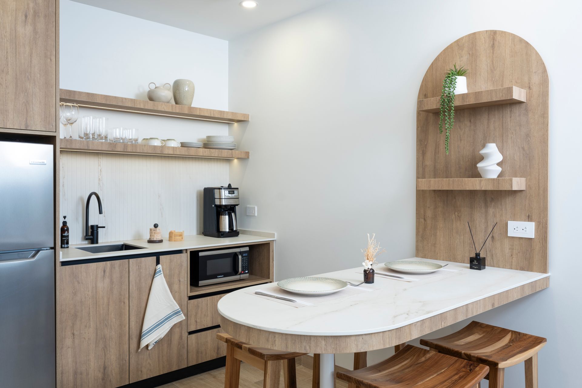 Bright minimalist kitchen and dining area with wood shelves, white island table, and black appliances