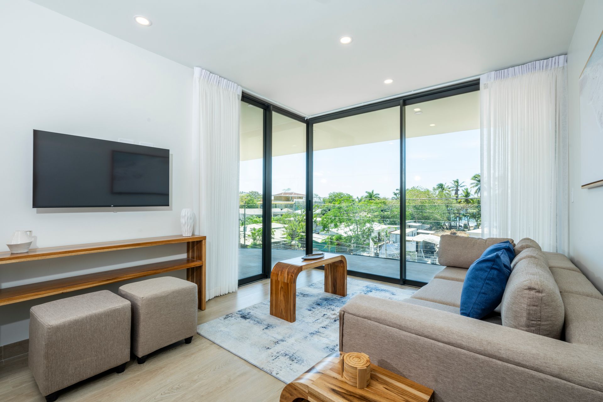 Bright modern living room with sofa, wall-mounted TV, and large windows overlooking water.