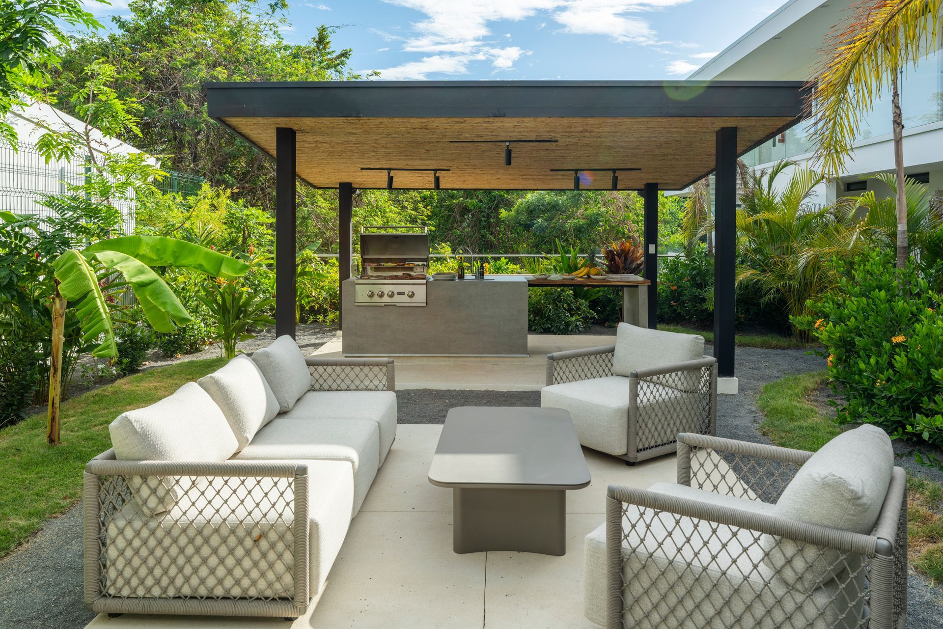 Modern outdoor patio with white sectional seating, a low table, and a shaded wood pergola in lush greenery