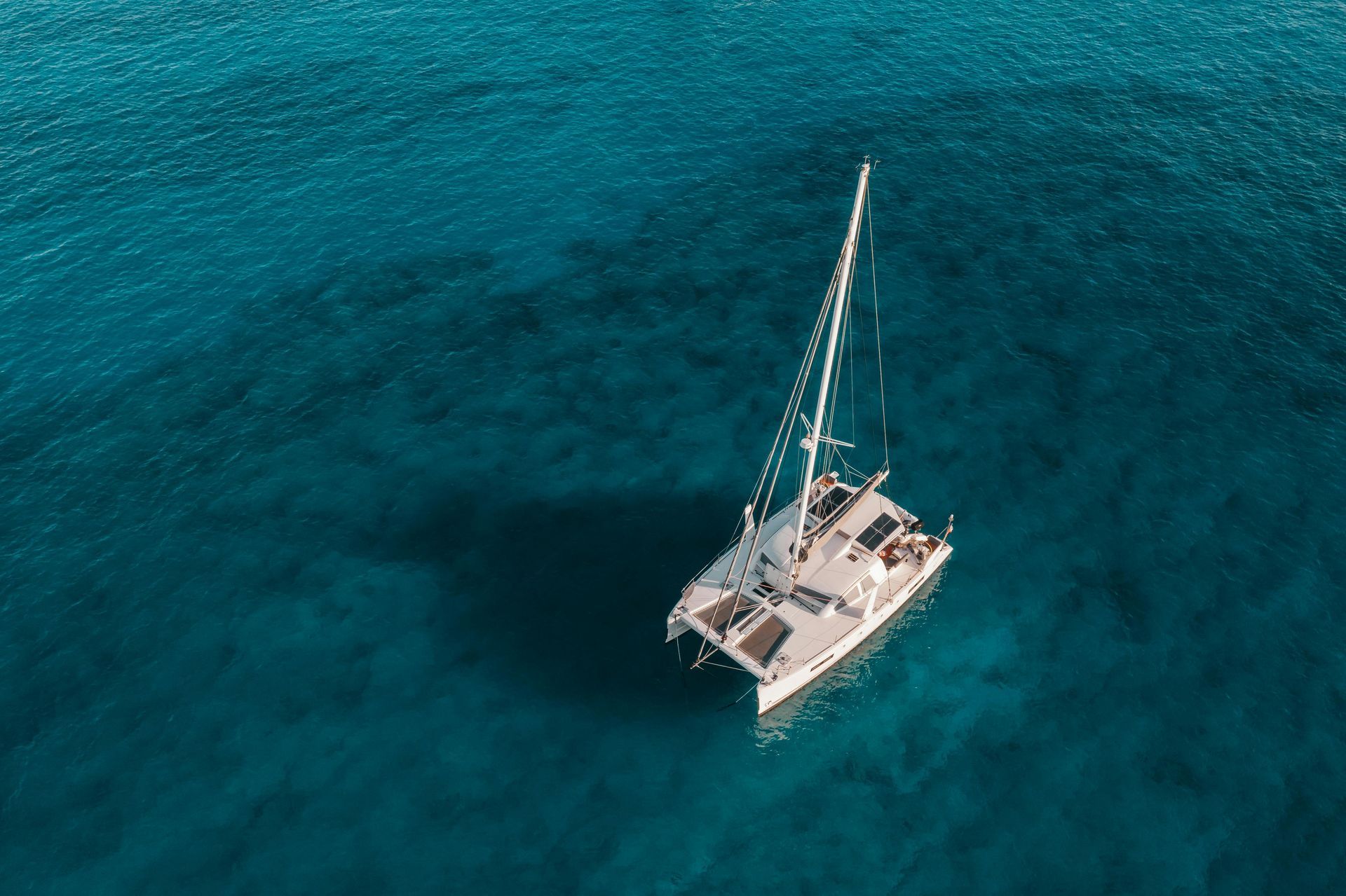 A white sailboat floating on bright turquoise ocean water, seen from above.