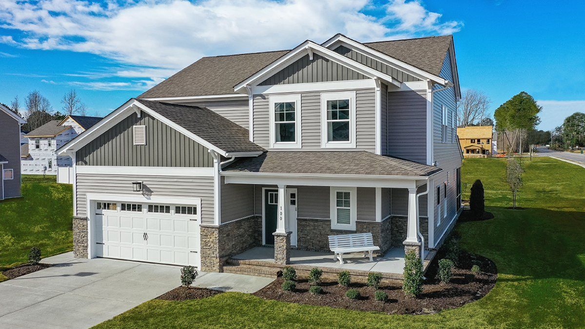 Two-story gray house with garage and porch, front yard with green grass, blue sky.