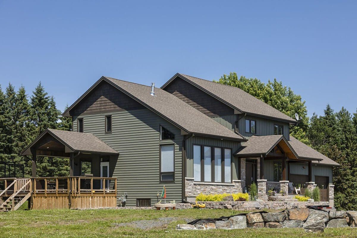 Two-story house with green siding, stone accents, and brown roof under a blue sky.