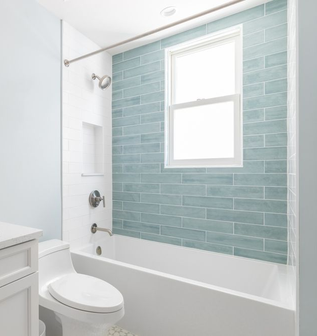 Bathroom with navy blue vanity, gold fixtures, and a white countertop. Doorway leads to a window.