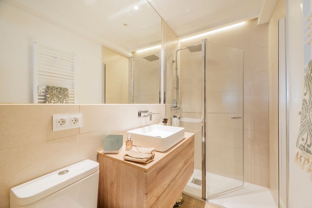 Modern beige bathroom with vanity, mirror, toilet, and glass-enclosed shower