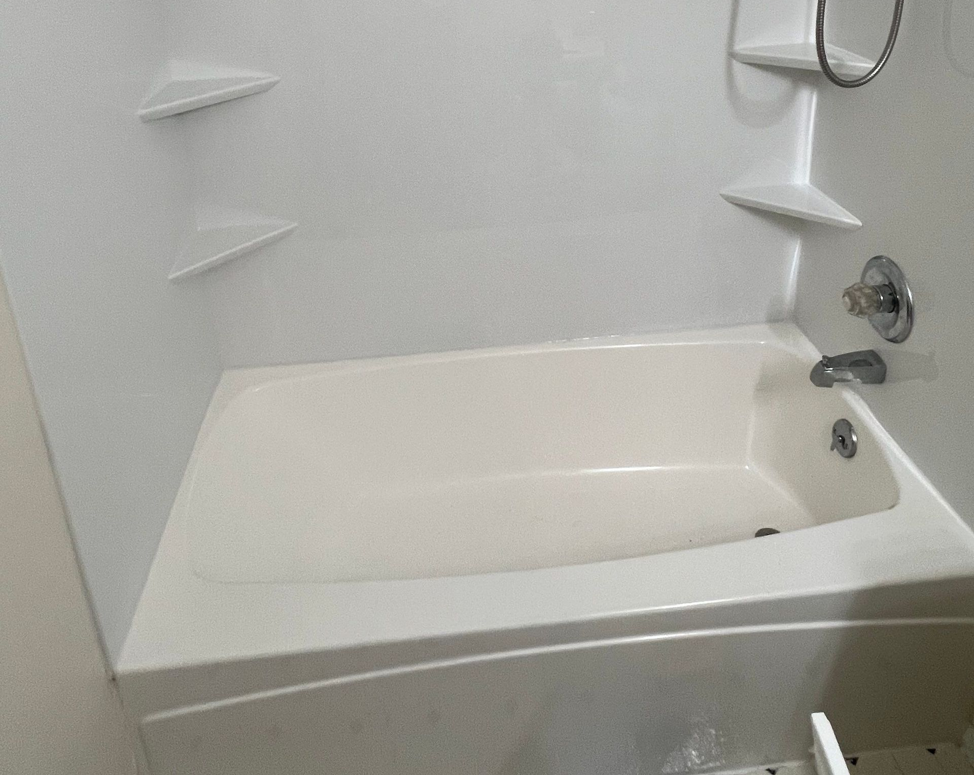 White bathtub in a small bathroom with a showerhead, faucet, and corner shelves above it