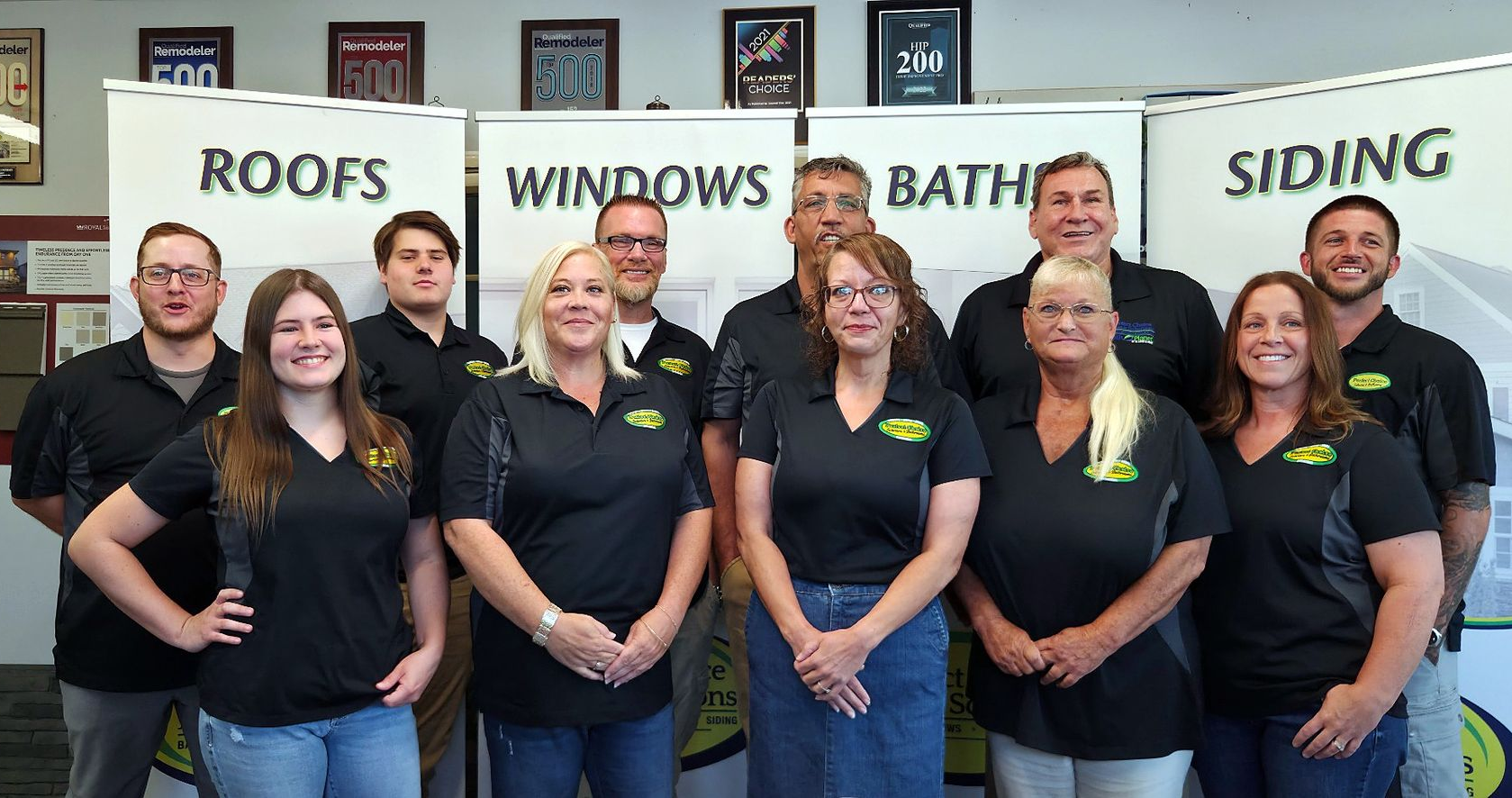 Team posing indoors in front of banners for roofs, windows, baths, and siding.