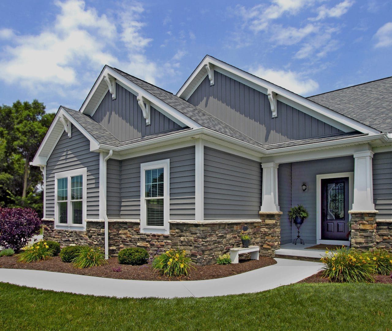Gray house with stone accents, white trim, and a blue sky.