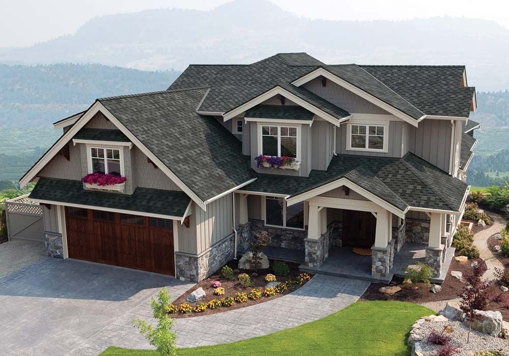 Gray house with dark roof, stone accents, and brown garage door, set in a hilly landscape.