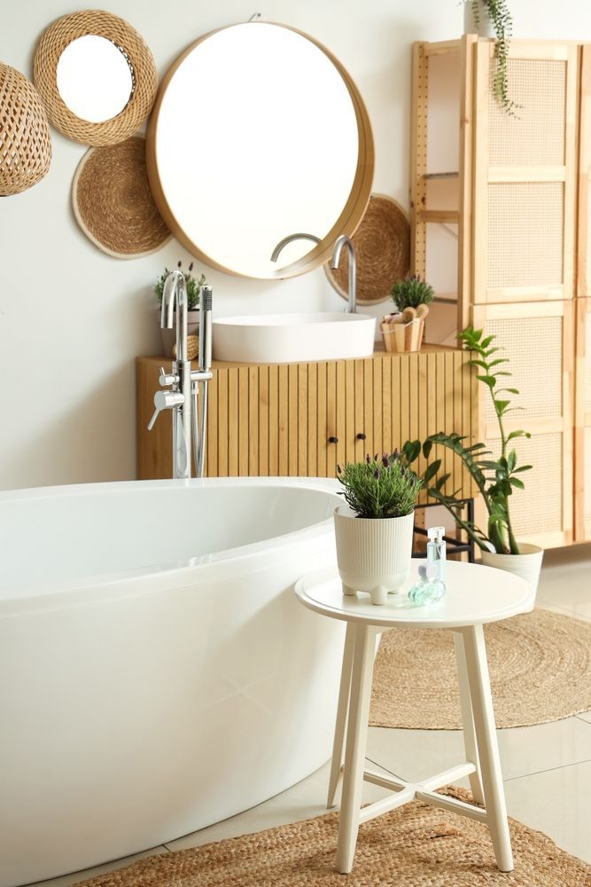 Bathroom with white tub, wooden vanity, round mirror, and woven decor.