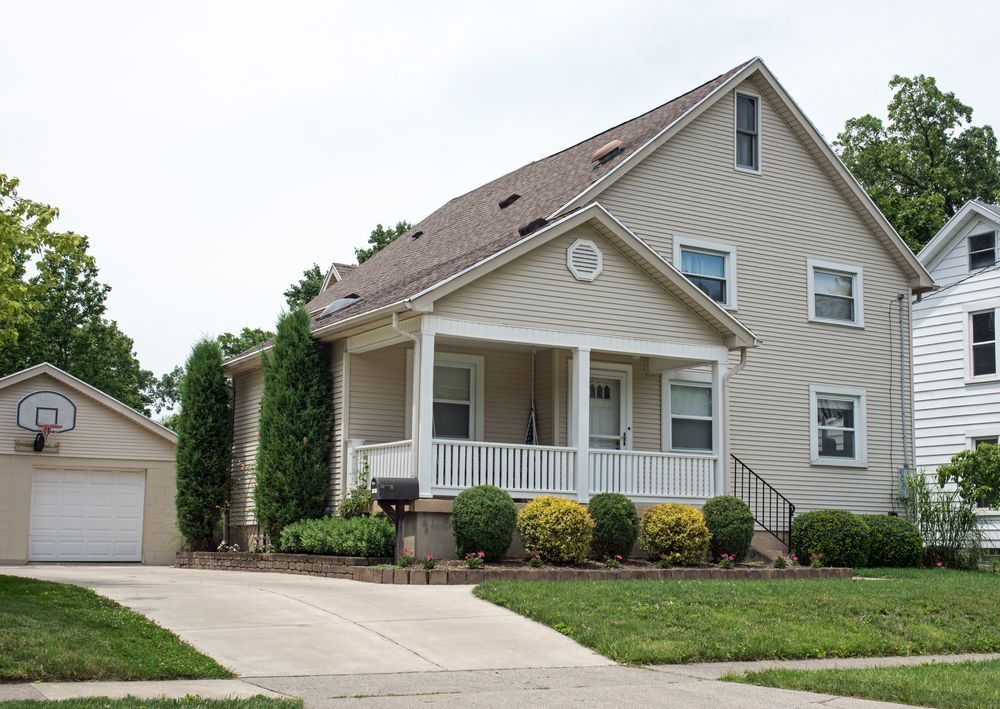 Beige two-story house with a porch and attached garage, on a green lawn.