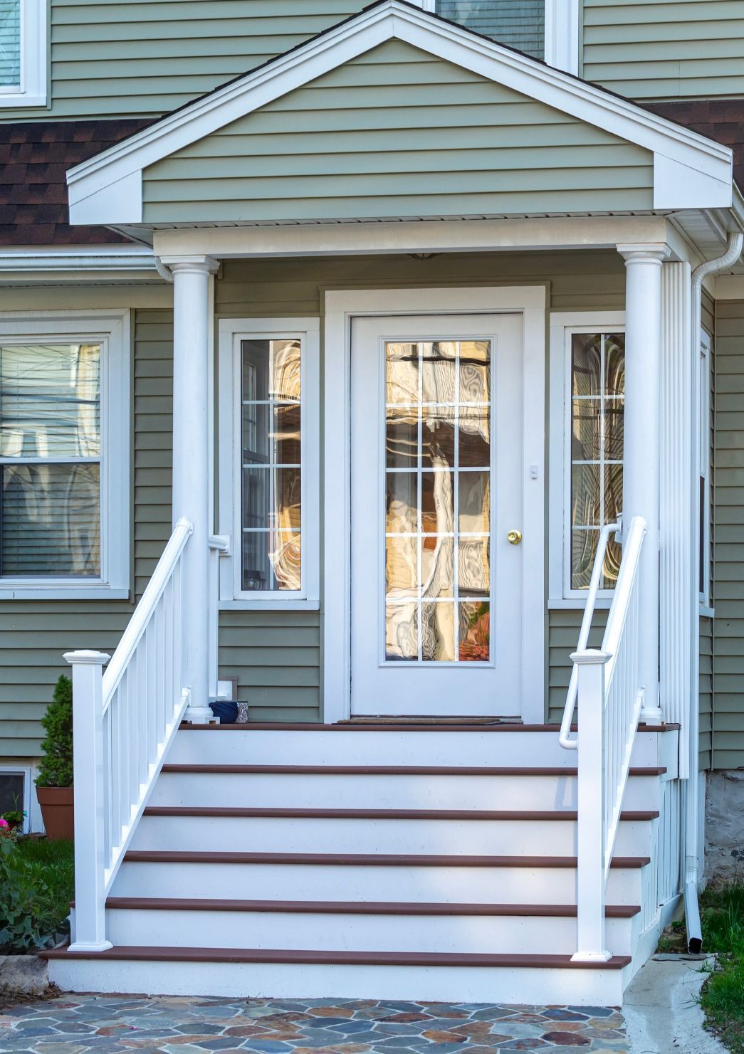 White front door and porch with steps, flanked by white columns, against a green siding house.