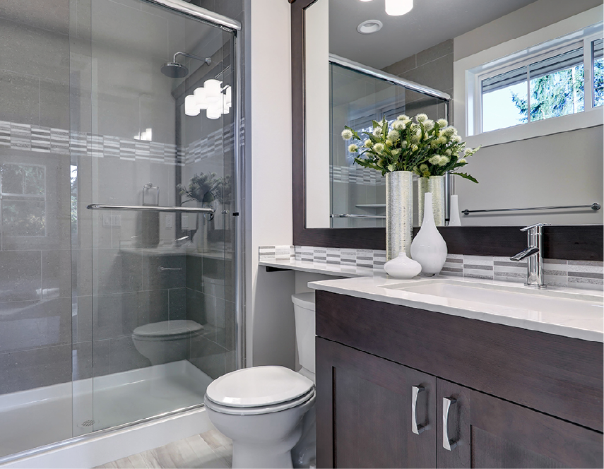 Bathroom with glass shower, toilet, dark-wood vanity, white countertop, and flowers in vase.