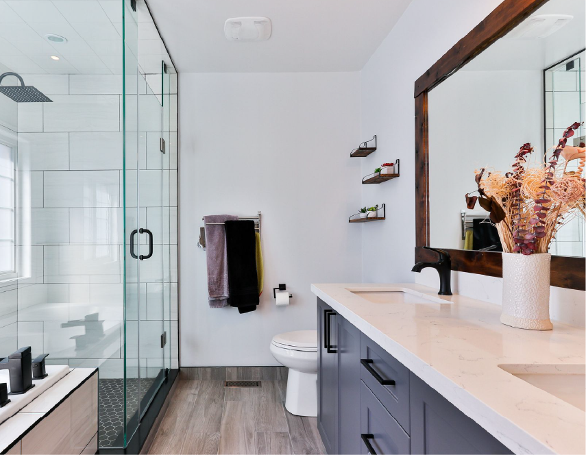 Modern bathroom with glass shower, white walls, gray cabinets, and wooden accents.