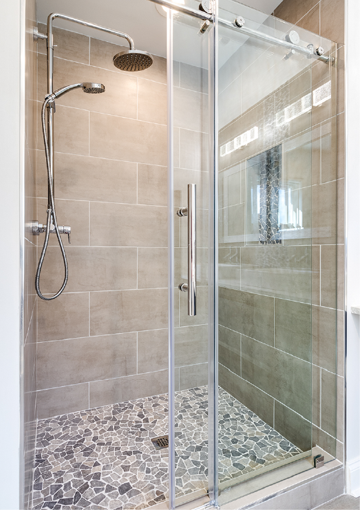 Glass-enclosed shower with pebble floor and stone tile walls; chrome shower head and handle.