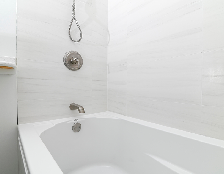 White bathtub in a tiled shower with silver faucet and showerhead.