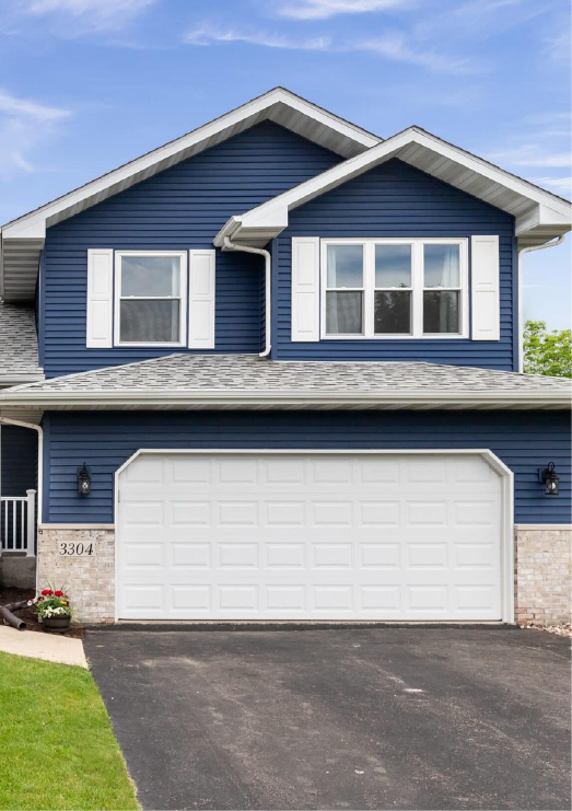 Blue house with white garage door and shutters. Asphalt driveway and green lawn.
