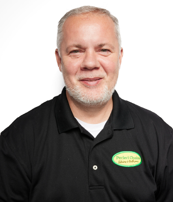 Man with graying hair and beard wearing a black polo shirt, smiling at the camera.