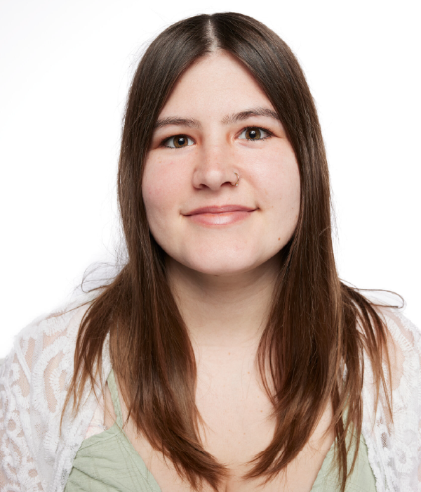 Woman with long brown hair smiling, wearing a white lace top and green shirt.