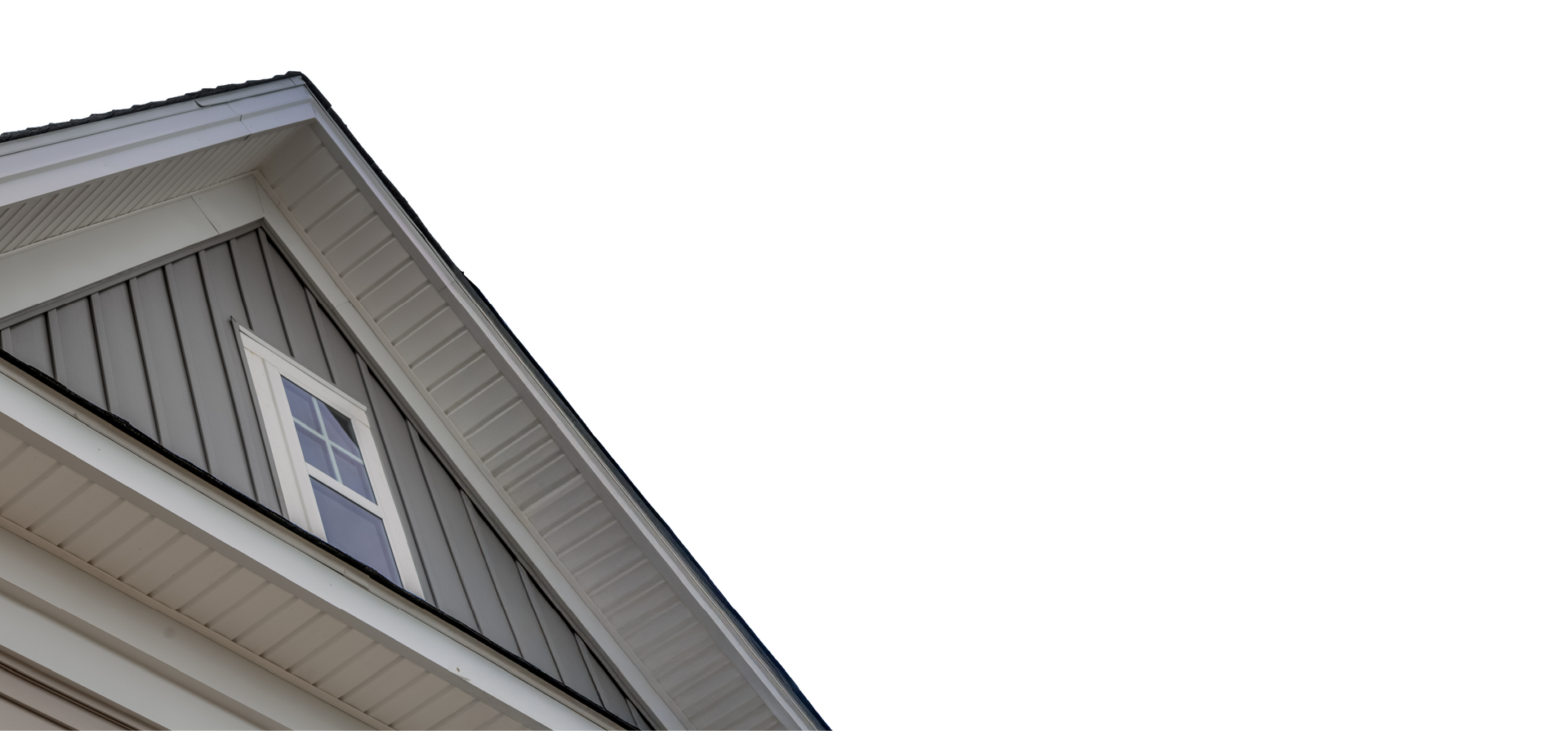 Exterior detail of a house roof with a small window. Gray and beige siding against a white sky.