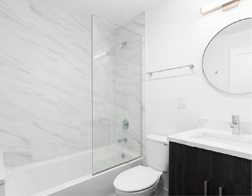 Bathroom with white marble-like tile, a glass shower panel, and dark wood vanity.