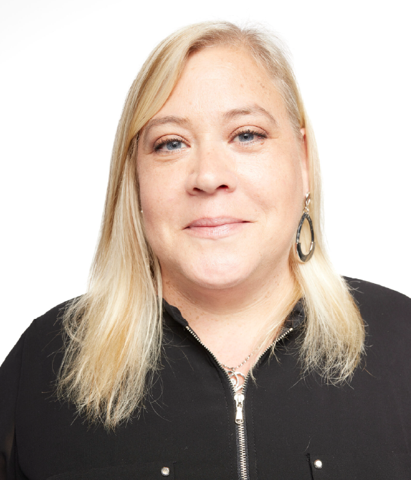 Woman with blonde hair wearing a black shirt, smiling at the camera. White background.