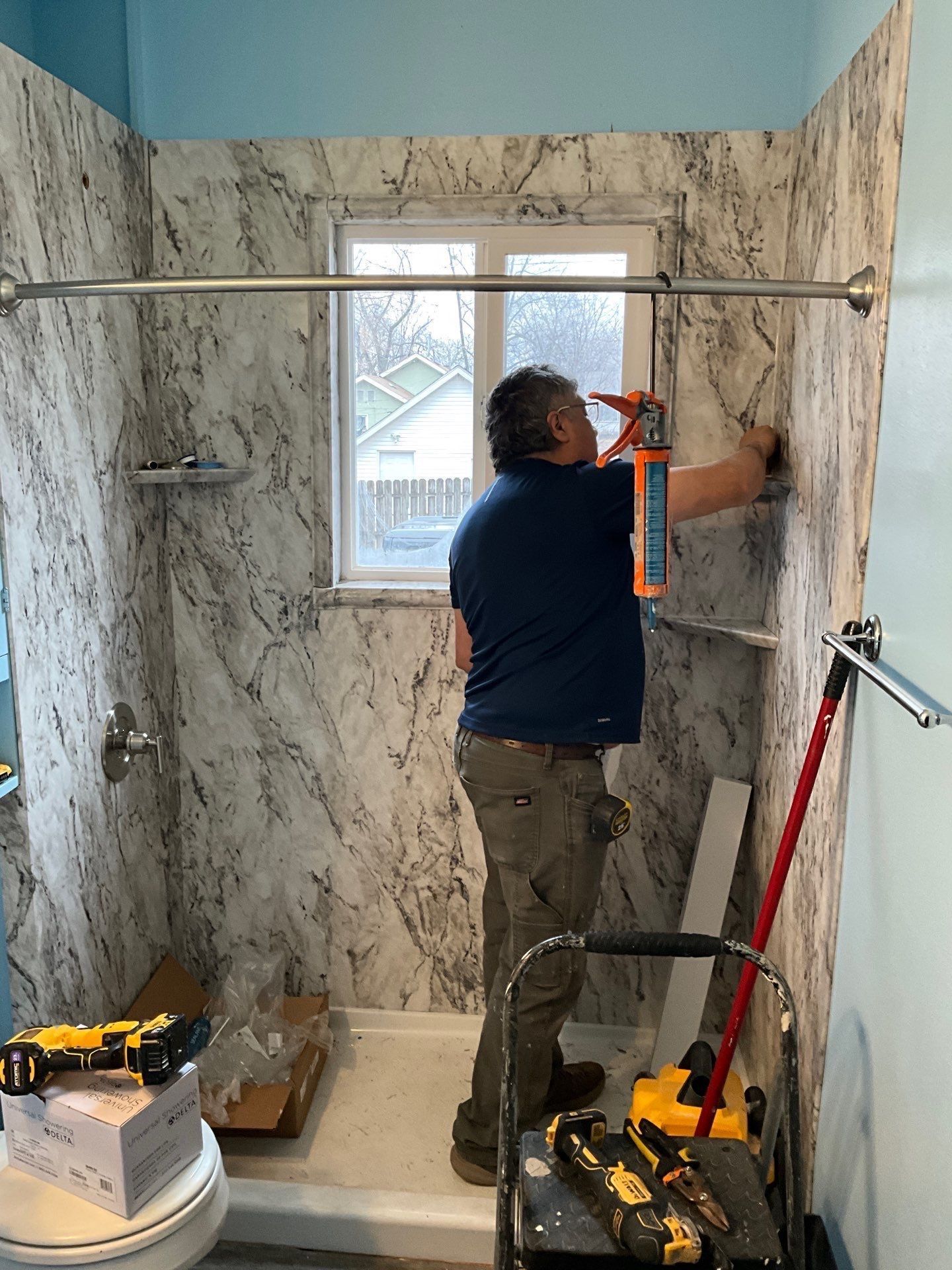 Person caulking around a bathtub in a bathroom, applying sealant with a caulk gun.