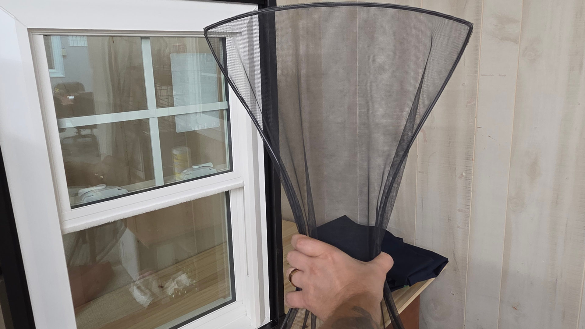 Hand holding a black FlexScreen near a window and light wood siding