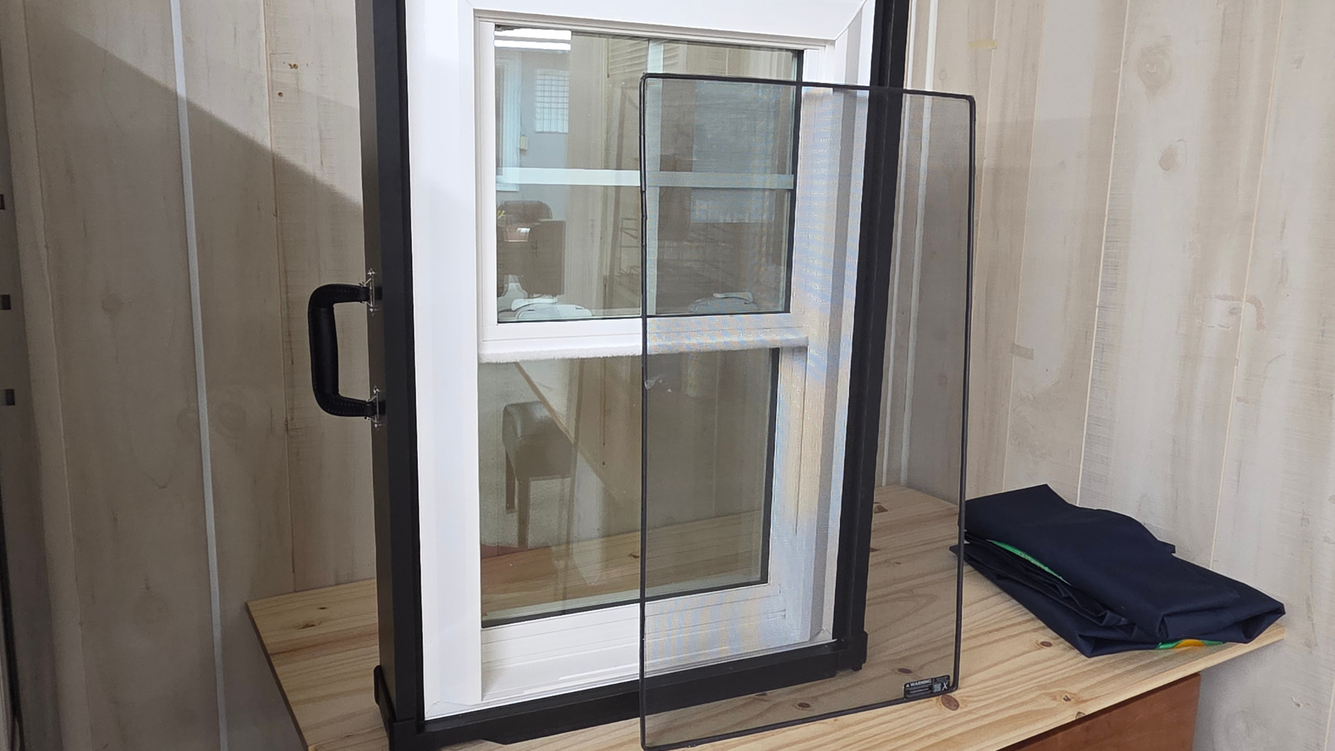 Black-framed window screen leaning on a table beside a folded cloth and curtain backdrop