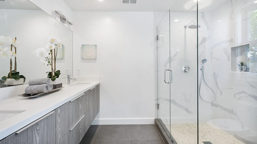 Modern bathroom with gray cabinets, white countertop, glass shower, and orchids.