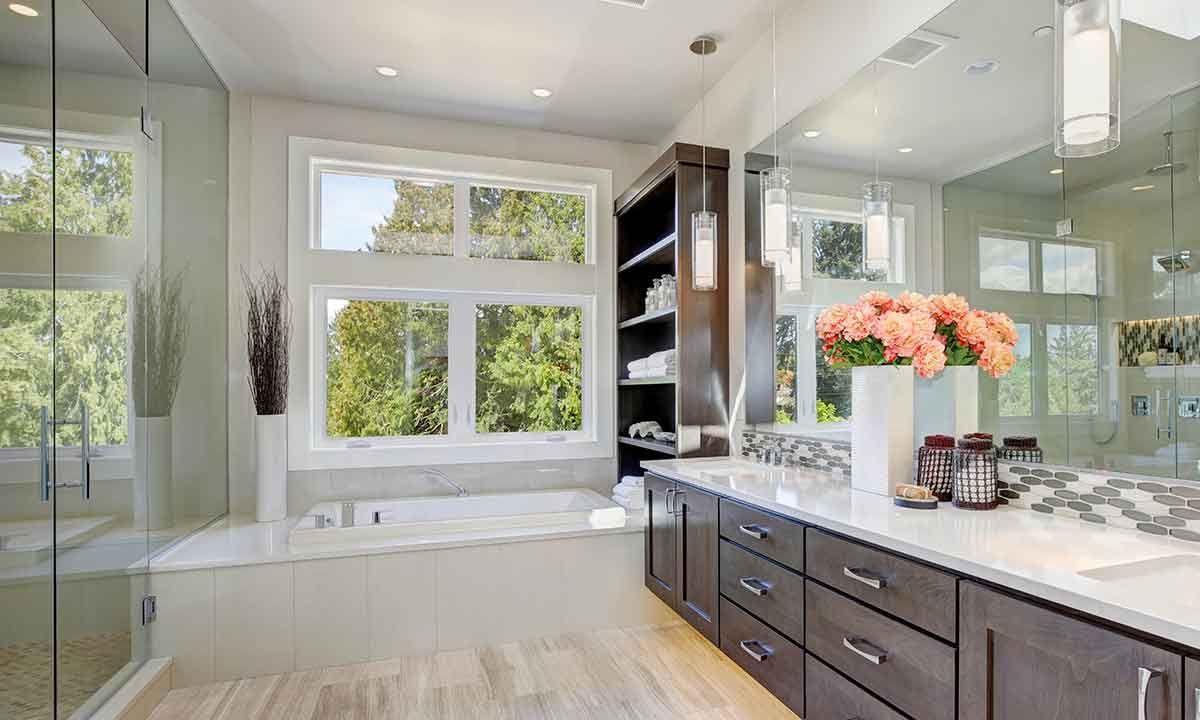 Luxurious bathroom with large windows, built-in shelving, dark wood vanity, white countertop, and flowers.