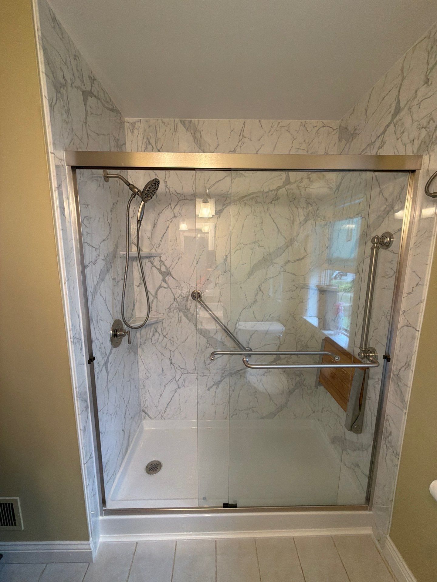 Modern glass walk-in shower with chrome fixtures, marble-look tile, and built-in corner bench.