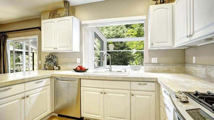 White kitchen with cabinets, a sink under a window, and a stainless steel dishwasher.