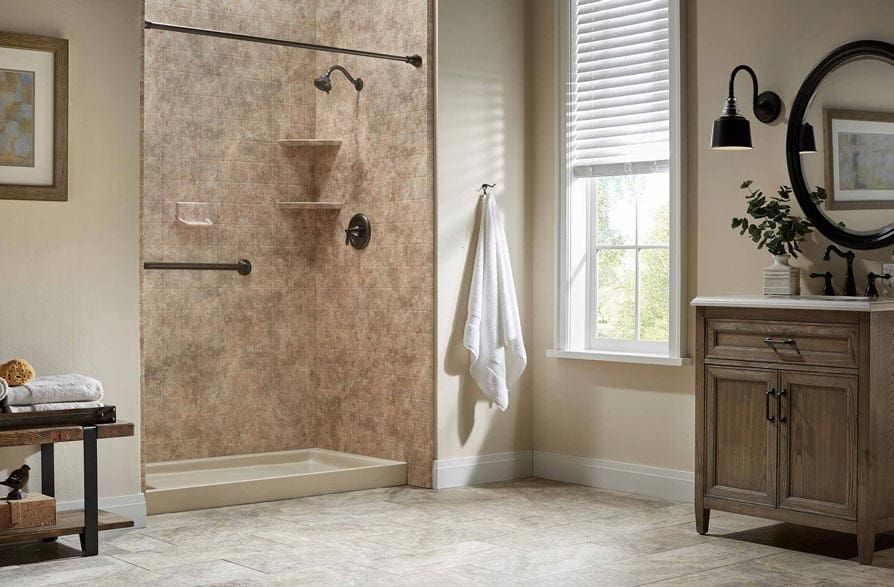 Bathroom with tan textured shower surround, shower seat, vanity, window, and rug.