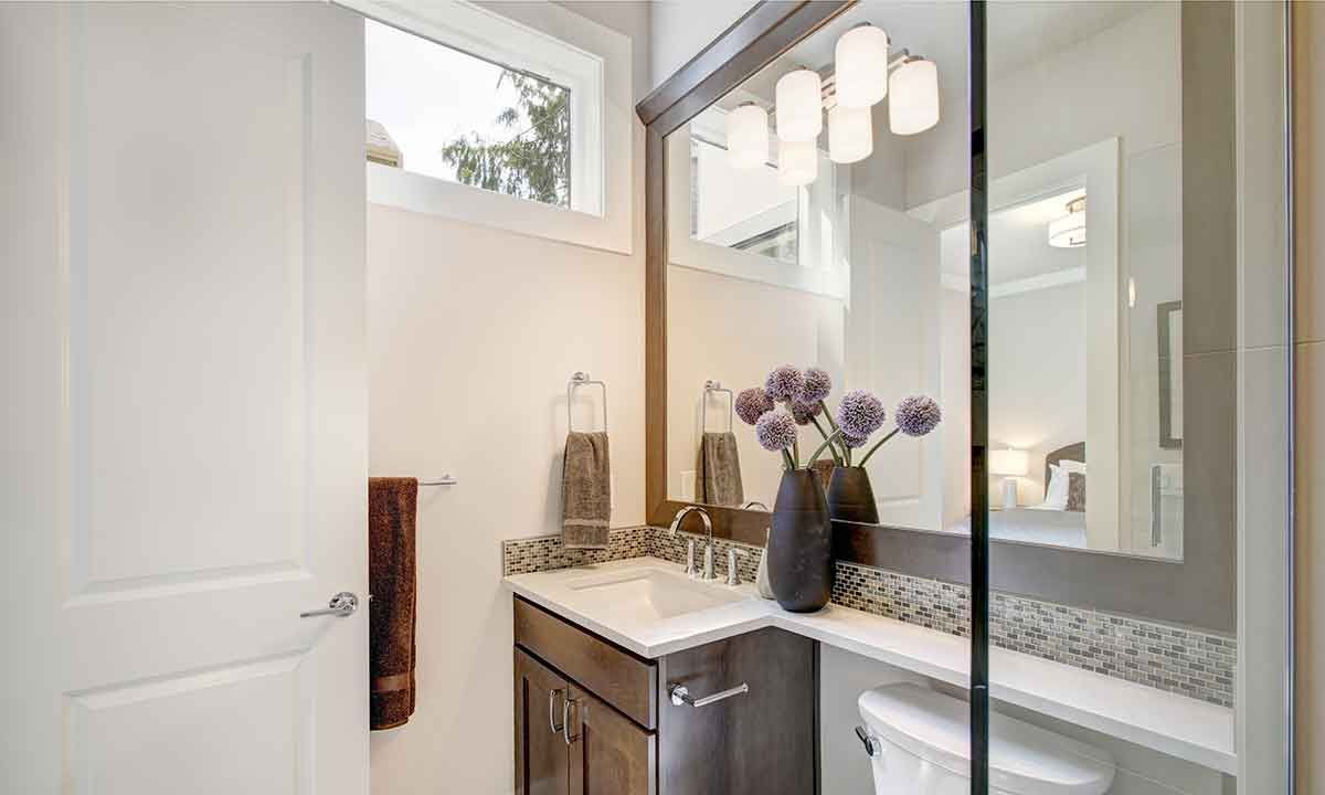 Bathroom with sink, mirror, toilet, and vase of flowers; white, brown, and gray tones.