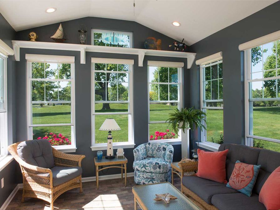Sunroom with gray walls, white windows, and wicker furniture overlooking a green yard.