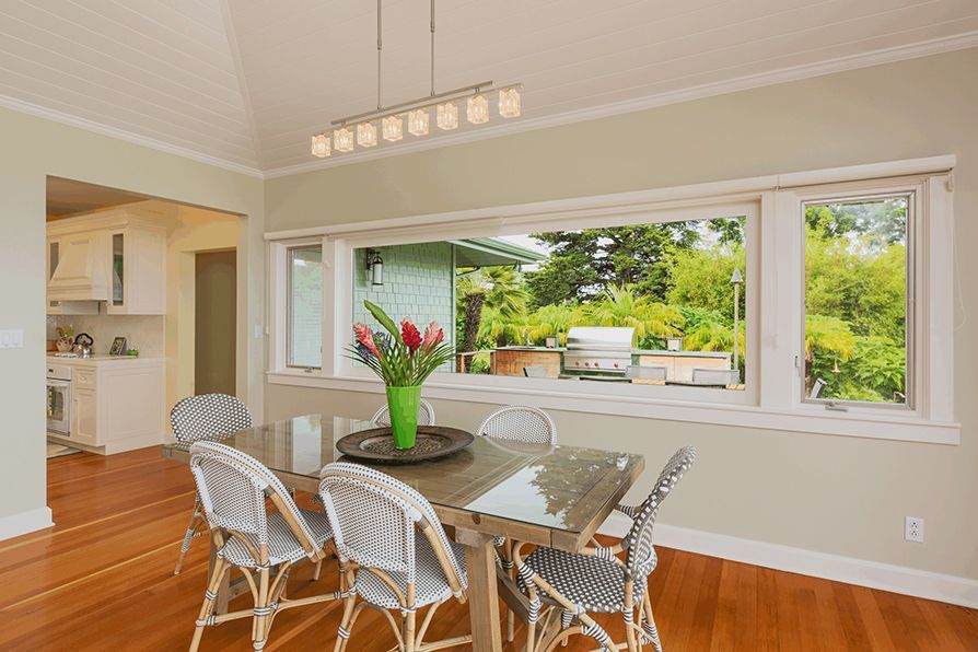 Dining room with a table, chairs, and large window overlooking greenery.