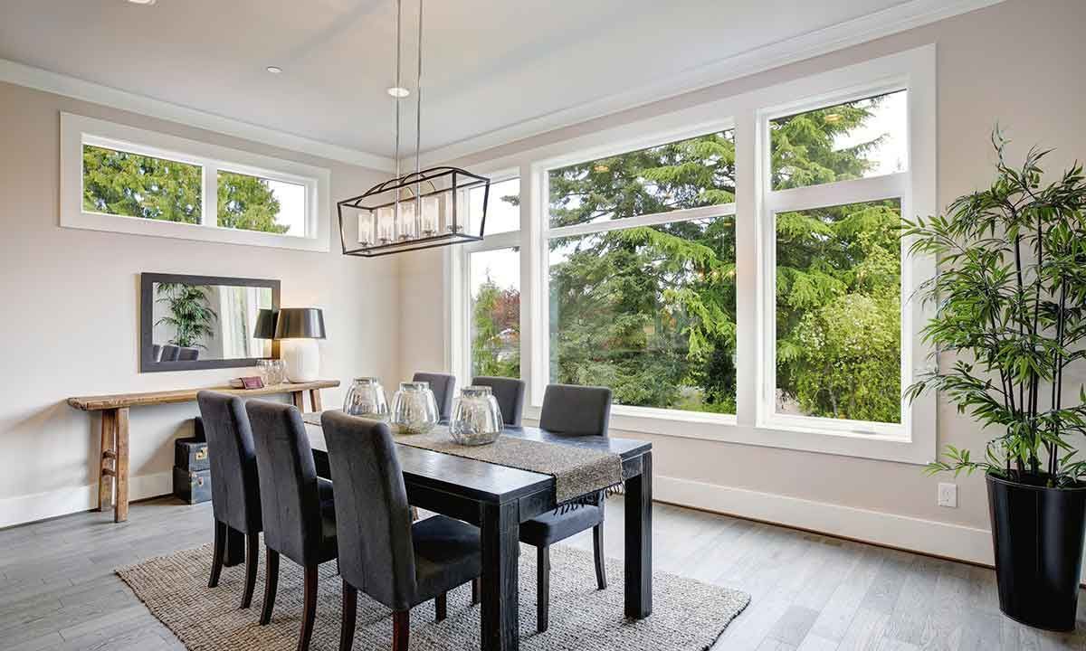 Dining room with black table, gray chairs, large windows overlooking trees, and a decorative light fixture.