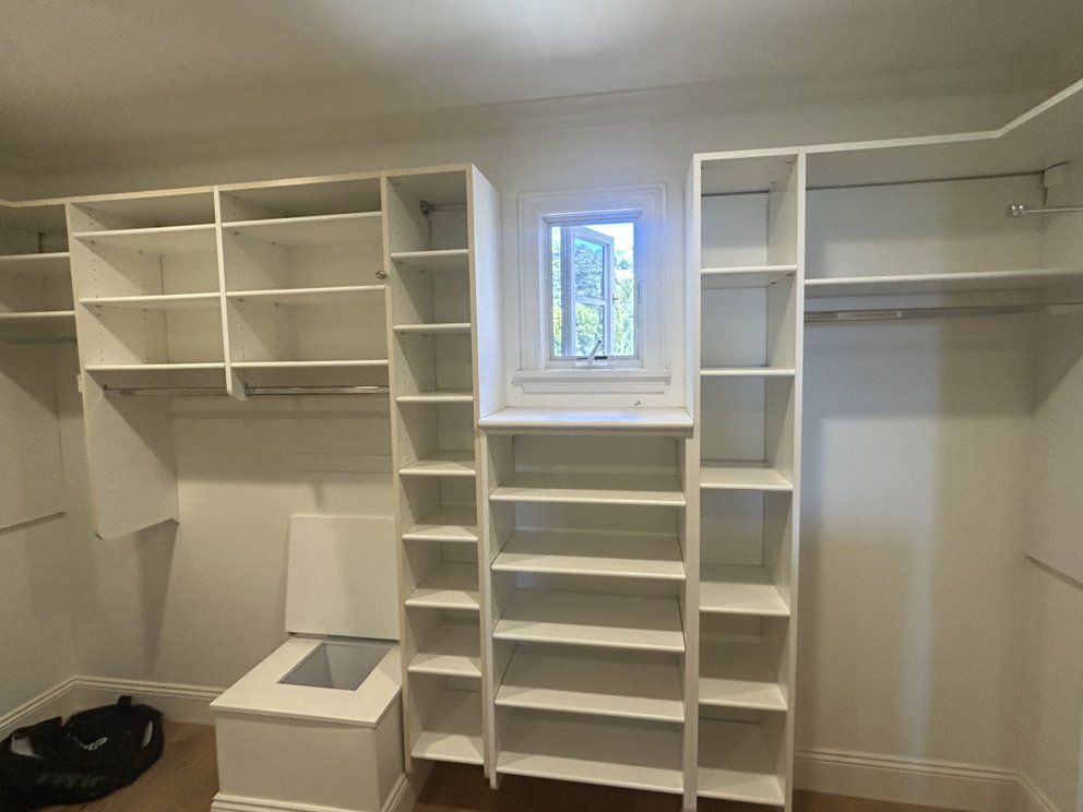 White closet with shelves, rods, and a small window in the center.
