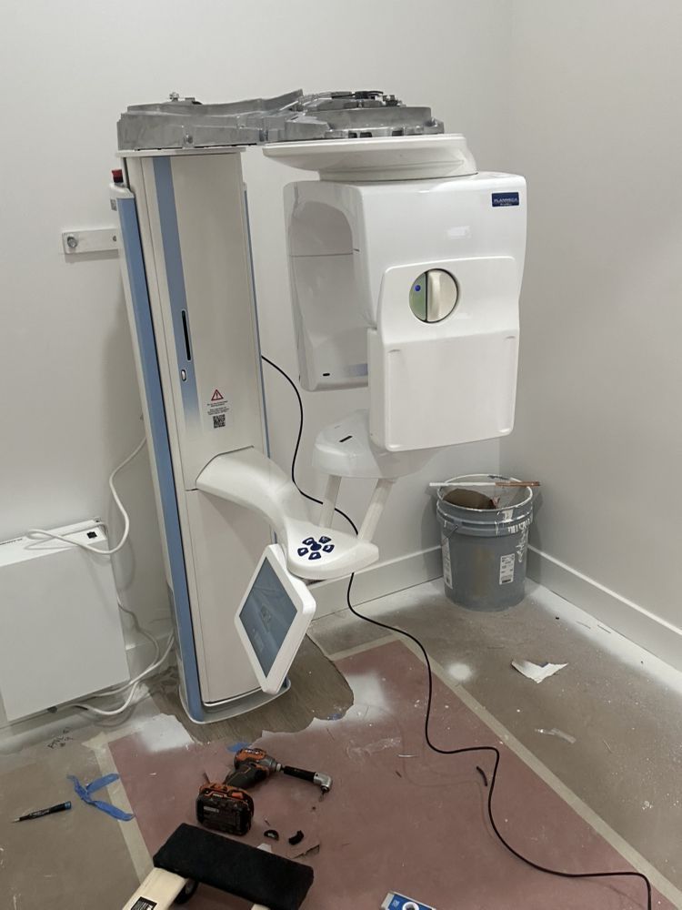 Dental X-ray machine in a room under construction. White and blue machine, tools, debris on floor.