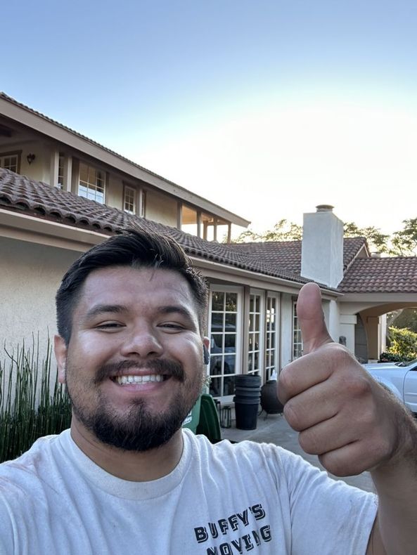 Smiling man with a thumbs-up in front of a house. He's wearing a light shirt and it’s daytime.