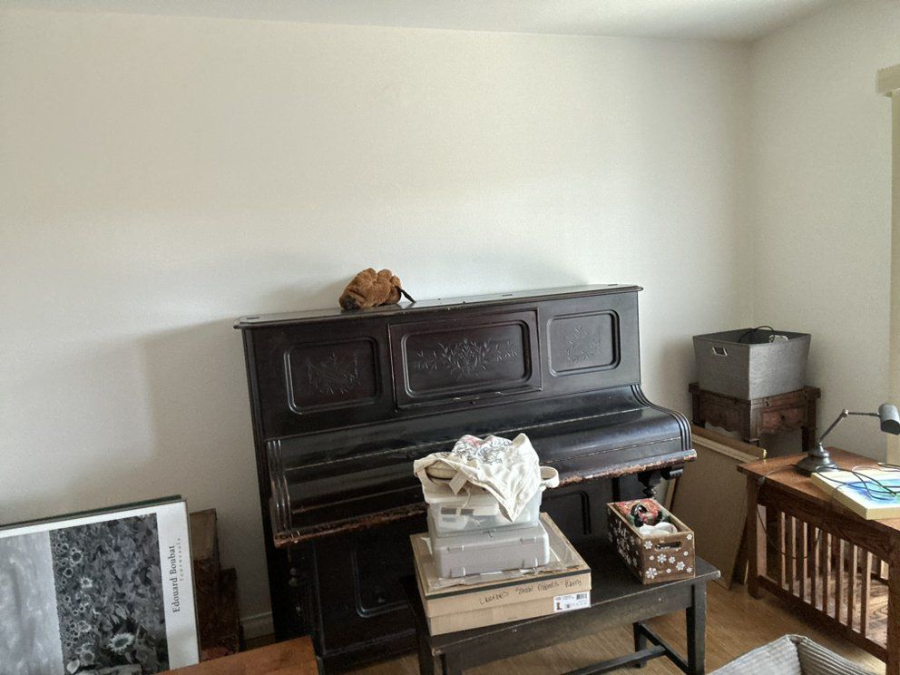 A dark wooden upright piano in a room with other objects, including a desk and boxes.