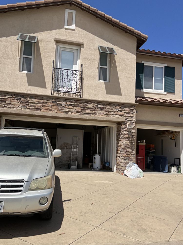 Two-story beige house with stone accents, attached garage, and a silver SUV parked in the driveway.