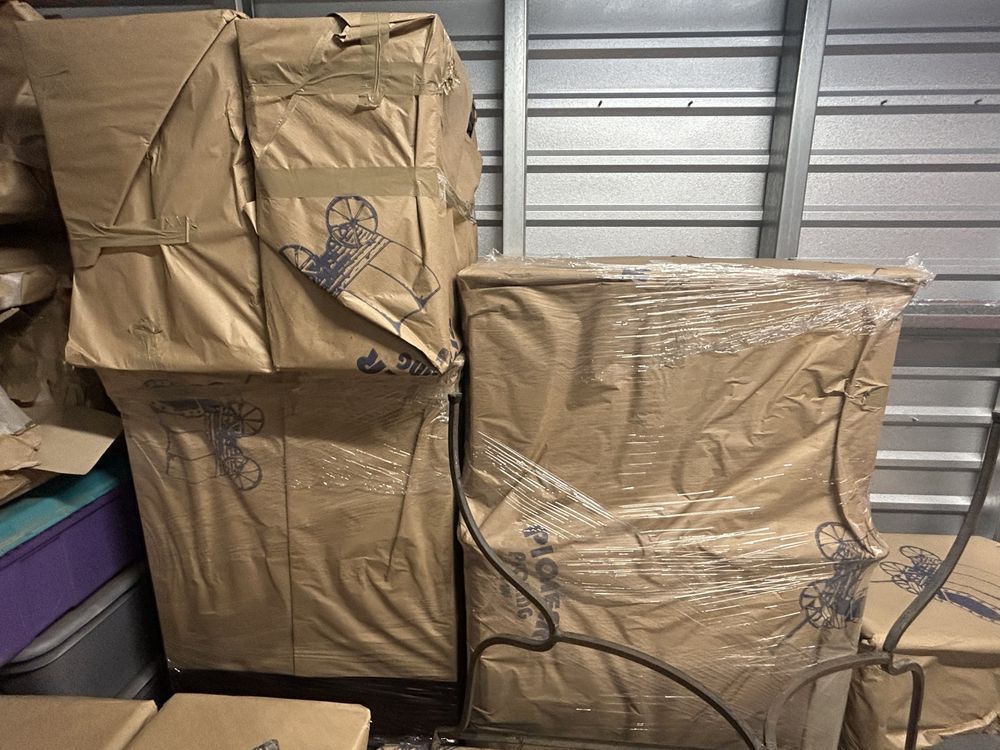 Boxes wrapped in brown paper and clear plastic stored in a metal-walled storage unit.