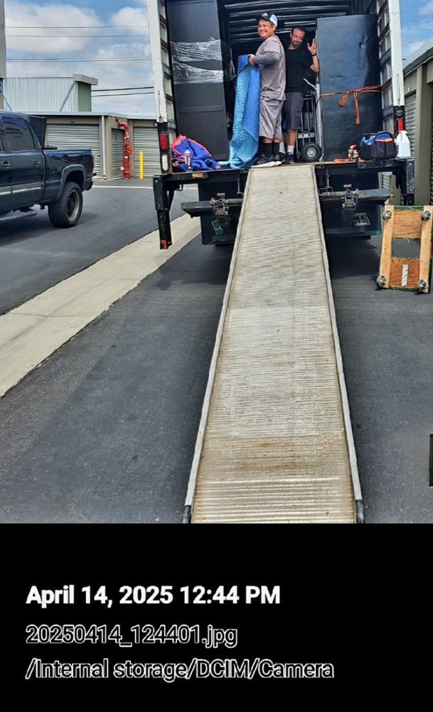 Movers loading a truck from a storage unit using a ramp.
