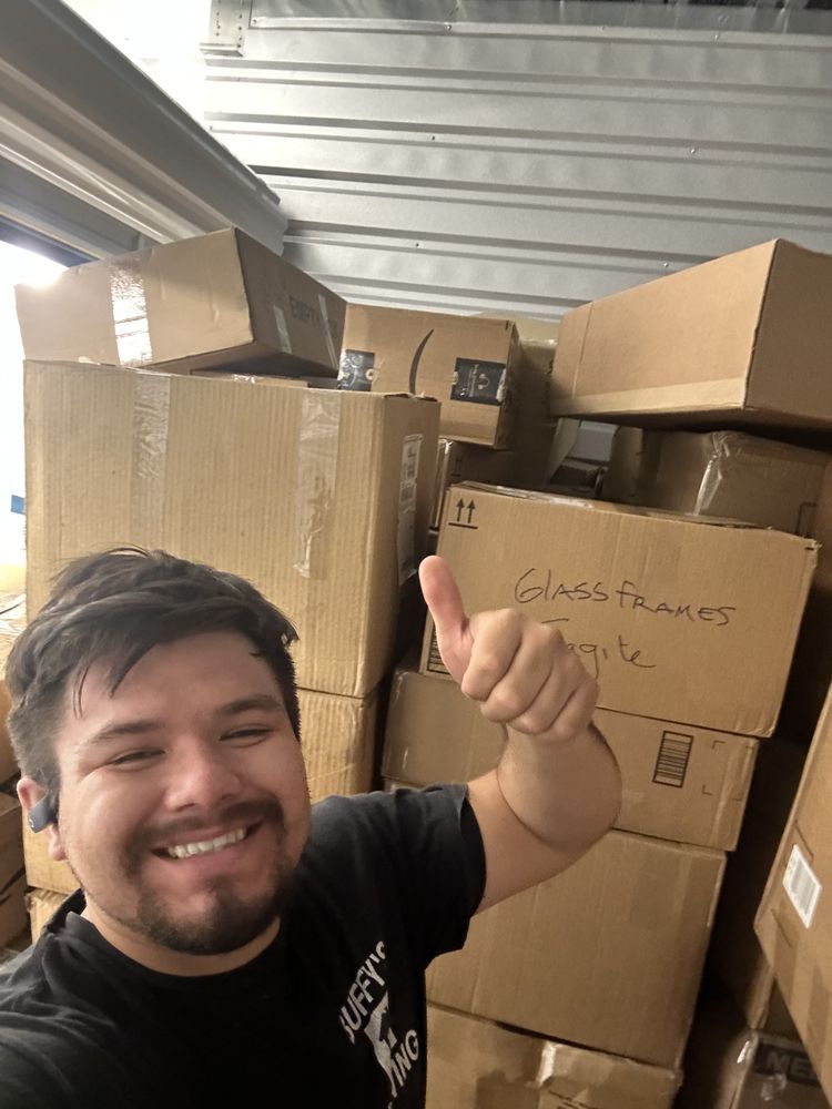 Man smiling, giving thumbs up, surrounded by many cardboard boxes in storage unit.