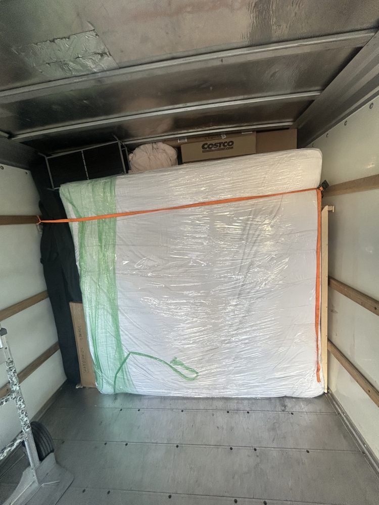 A wrapped mattress secured in a moving truck with straps and other items stored inside.