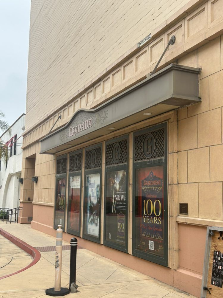 Theater exterior with posters, a canopy, and a light-colored brick facade.