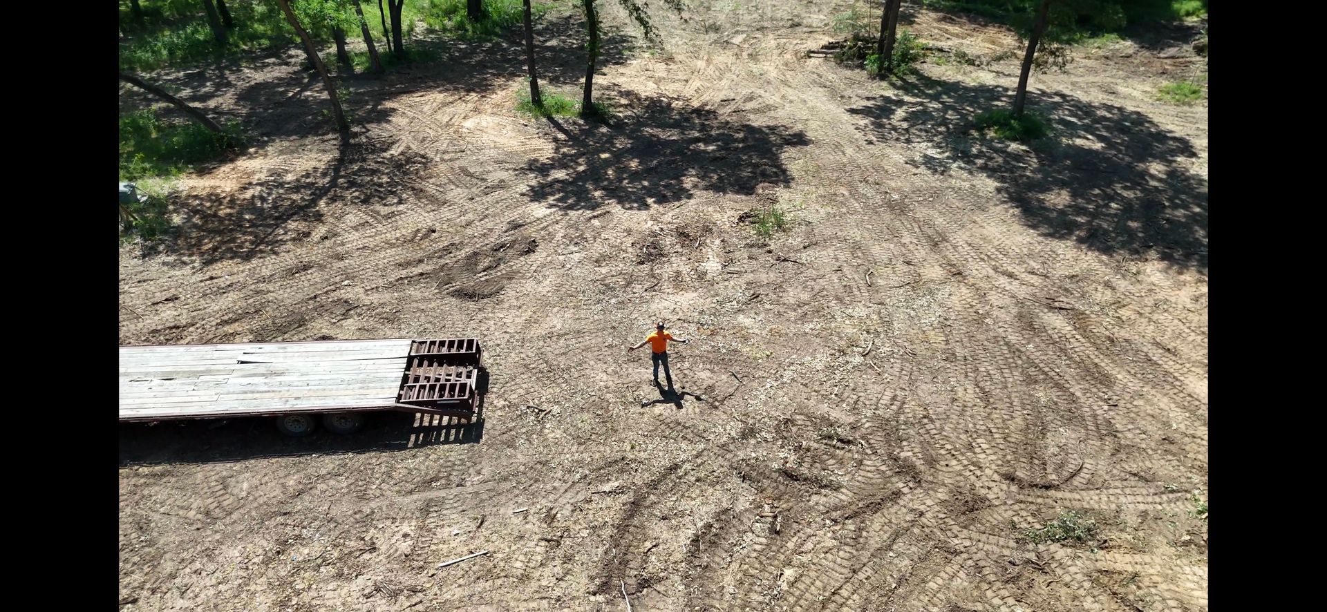 An aerial view of a cleared lot with a flatbed trailer and a person standing in the center.