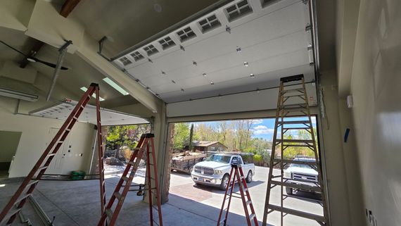 Garage under construction with ladders, open garage door, and parked car outside.